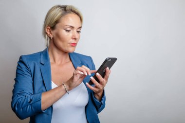 Genç bir kadın, sarışın, akıllı telefon mesajları yazıyor, stüdyo, beyaz arka plan.