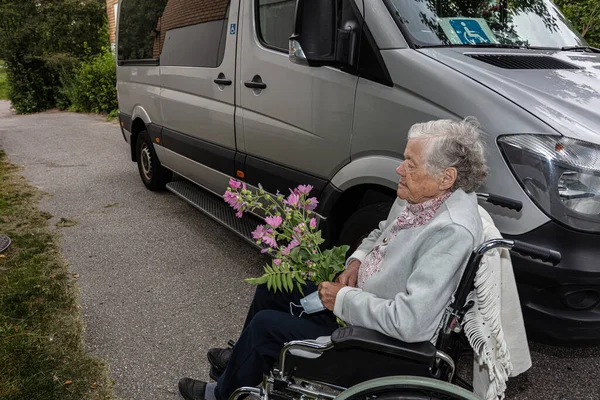 Elderly woman holding a medical mask with flower Concept of a disabled person in a wheelchair transporting patients in a car. — Stock Photo, Image