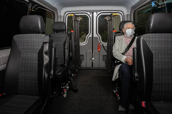 Elderly woman in a medical mask, in a car for transportation of disabled people, the concept of transportation of patients in the car.