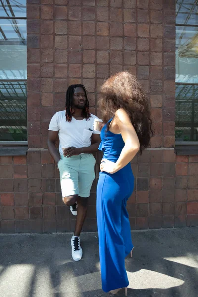 african man and european caucasian woman drinking coffee from paper cups. summer day, outdoor