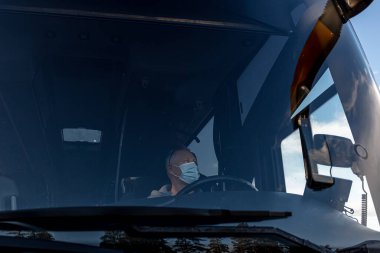 Sağlık maskesi takan otobüs şoförü, ön camdan salgın sırasında güvenli sürüş yapıyor, Coronavirus 'a karşı koruma sağlıyor.