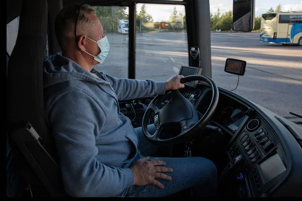 Bus driver wearing a medical mask, looking out of the bus window Safe driving during a pandemic, protection against coronavirus