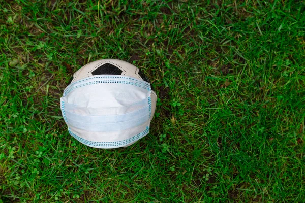 A fű hátterére orvosi maszk van a labdán, szövegnek helye van. A gyermekek koronavírus elleni védelme — Stock Fotó