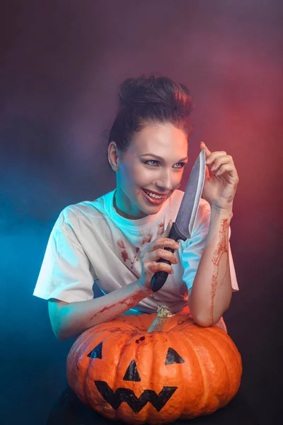 Donna ricoperta di sangue con un coltello, capelli scuri e una zucca - concetto di Halloween. — Foto Stock