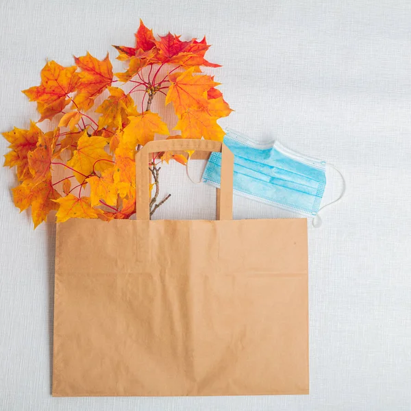 Maple leaves, a paper bag and a medical mask. On white background. View from above . There is room for text. Autumn layout. Horizontally