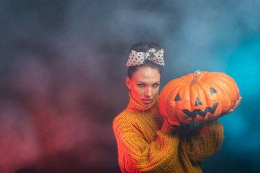 Puantiyeli bir esmer ve elinde balkabağı tutan sarı bir süveter. Stüdyonun karanlık arka plan Cadılar Bayramı konseptinde. Metin için bir yer var