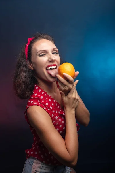 Brunette with an orange. Studio, dark background She is holding a fruit in her hand. — Stock Photo, Image