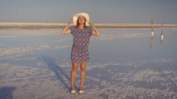 Λεπτή σέξι κορίτσι στο λευκό καπέλο, απολαμβάνοντας το ηλιοβασίλεμα, ξύλινα αλάτι πυλώνες από μια λίμνη αλατιού — Αρχείο Βίντεο