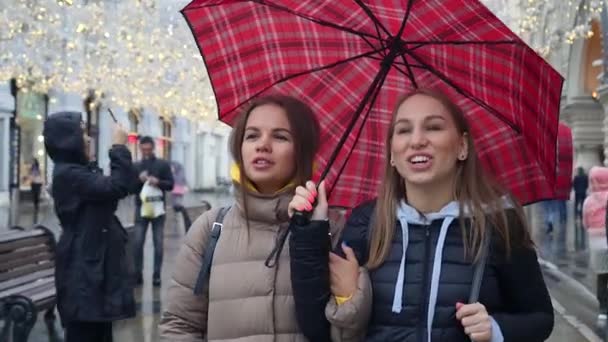 Dua sahabat wanita berjalan di jalan Nilolskaya dengan payung merah — Stok Video