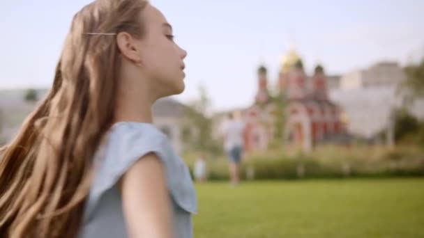 Charmant langharig meisje in een blauwe jurk spin in dans in een stadspark in de zomer — Stockvideo