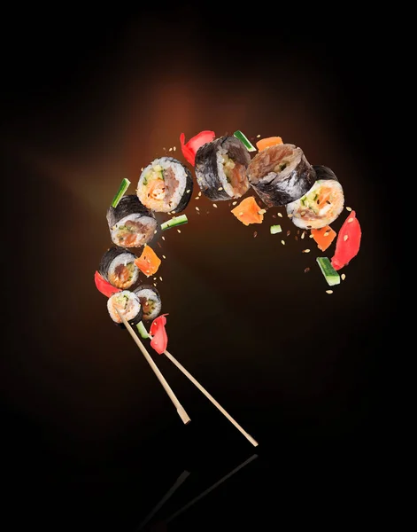 Čerstvé sushi rohlíky s hůlkami, zmrazené ve vzduchu na černém pozadí — Stock fotografie