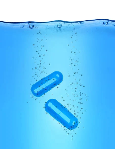 两个医疗胶囊溶解在蓝水中 — 图库照片