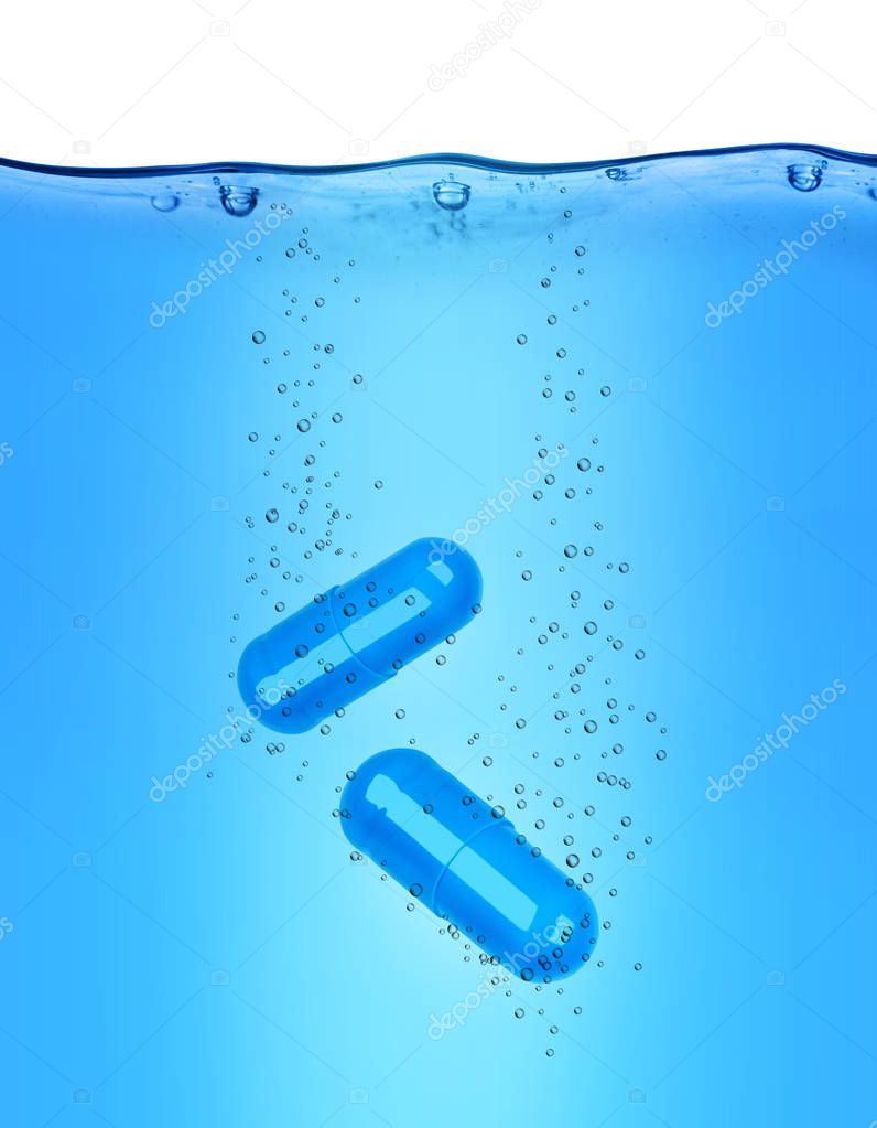 Two medical capsules dissolves in blue water