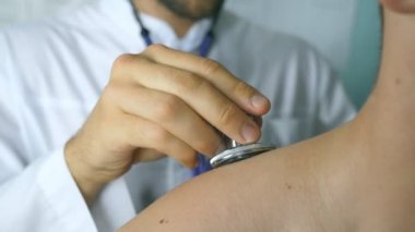 Doktor muayene genç erkek hasta stetoskop ile. Göğüs Hastanesi ofisinde bir adam kontrol doktor. Tıbbi işçi dinleme kalp atışı bir adam. Arka arka görünümü kapatın