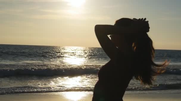 Junge brünette Frau bindet Pferdeschwanz am Strand in der Nähe des Meeres bei Sonnenuntergang. schöne Mädchen pressen ihre Haare am Meeresufer bei Sonnenaufgang. Touristinnen flechten Haare und machen Frisuren. Haarpflege-Zeitlupe — Stockvideo