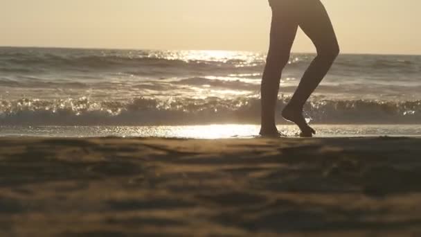 Nogi młodej kobiety stąpającej po piasku. Zbliżenie żeńskich stóp spacerujących po złotym piasku na plaży z falami oceanicznymi w tle. Boso dziewczyna na brzegu morza. Wakacje. Zwolniony ruch — Wideo stockowe