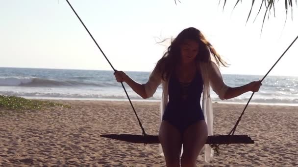 Šťastná dívka v plavkách a tričko relaxační na houpačce na pláži tropického oceánu. Krásná dívka sedí na houpačce a užívat si letních prázdnin nebo dovolené. Žena baví na moři pobřeží. Zpomalený pohyb — Stock video