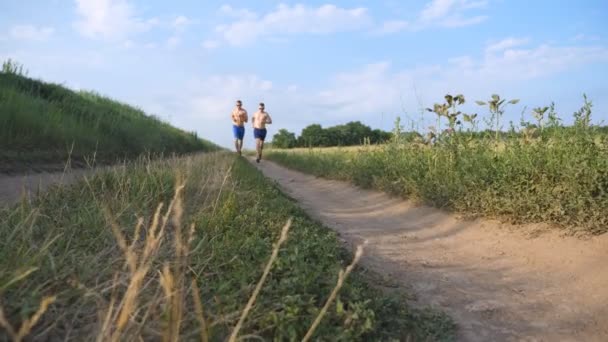 Dos hombres musculosos corriendo y hablando al aire libre. Jóvenes deportistas corriendo por el campo. Hombres deportistas entrenando juntos en la naturaleza. Amigos haciendo ejercicio afuera. Estilo de vida activo saludable en cámara lenta — Vídeos de Stock