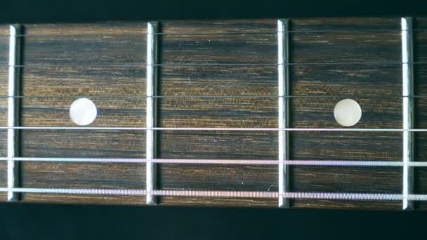 Primer plano de la cuerda de la guitarra vibrando durante el juego. Cordón rasguñado y viéndolo vibrar. Temblando contra el traste. Hermoso fondo con textura de madera. Actuación musical. Movimiento lento — Vídeos de Stock