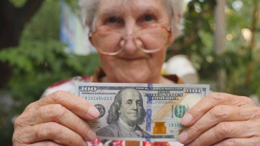 Yüz dolarlık banknot kameraya açık gösteren gözlük yaşlı kadın. Mutlu Büyükanne dışındaki yabancı para tutuyor. Para kavramı. Yavaş hareket kapatmak