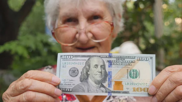 Yaşlı kadın ve açık gülümseyen yüz dolarlık banknot kameraya gösteren gözlük. Mutlu büyükanne dışındaki yabancı para tutuyor. Para kavramı. Yavaş hareket kapatmak