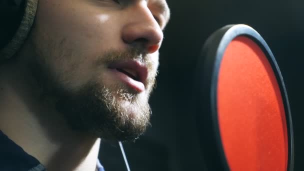 Primer plano de cantante masculino en auriculares cantando canción en el micrófono en el estudio de sonido. Joven grabando emocionalmente una nueva canción. El trabajo del músico creativo. Concepto del negocio del espectáculo. Movimiento lento — Vídeo de stock