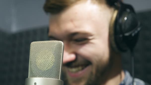 サウンド スタジオで作業中に笑みを浮かべてのヘッドフォンで男性歌手の肖像画。若い男は感情的に新曲を録音します。創造的な音楽家の働き。ショー ビジネスのコンセプトです。スローモーション — ストック動画