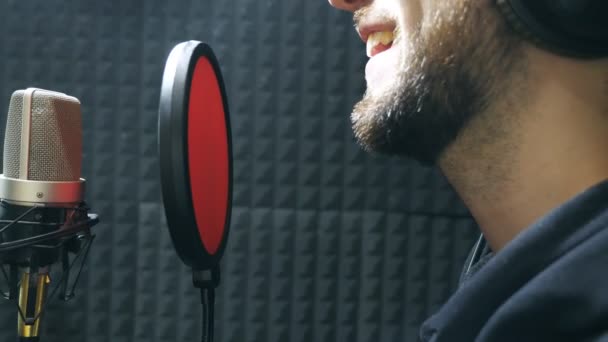 Cantante masculino en auriculares cantando canción en el micrófono en el estudio de sonido. Joven grabando emocionalmente una nueva canción. El trabajo del músico creativo. Concepto del negocio del espectáculo. Vista lateral en cámara lenta — Vídeo de stock