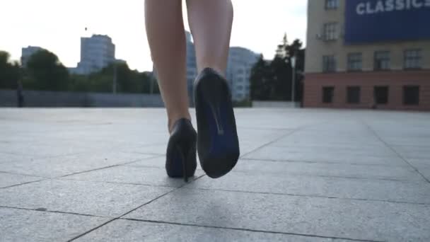 跟随女性腿在高跟鞋在城市街道走。年轻的商业妇女的脚在高高跟鞋的鞋去城市。女孩踏入工作。慢动作特写后向后视图 — 图库视频影像