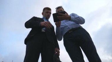 İki genç işadamları bahsediyoruz ve kullanarak tablet pc açık. İş erkek dışında dijital tablet ile gökyüzü arka plan üzerinde çalışıyor. Mobil teknoloji uygulayarak iş arkadaşları. Düşük görüş yavaş hareket açısı