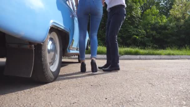 Man wordt geopend en de deur van oude auto in petto heeft voor de mooie jonge vrouw in hoge hakken schoenen. Guy openen deur van vintage auto voor vrouwelijke passagier. Meisje krijgen in retro auto. Slow Motion — Stockvideo