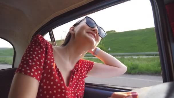 Ευτυχισμένο κορίτσι με γυαλιά ηλίου κλίνει έξω από ρετρό παράθυρο του αυτοκινήτου και να απολαύσετε το ταξίδι. Νεαρή γυναίκα κοιτάζει έξω από το παράθυρο της κίνησης παλιά αντίκα auto την ηλιόλουστη μέρα. Σχέδιο ταξιδιού και ελευθερίας. Αργή κίνηση Κλείσιμο — Αρχείο Βίντεο