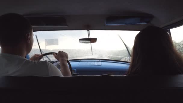 Casal jovem montando no carro vintage durante o tempo chuvoso. Homem e mulher irreconhecíveis sentados no banco da frente do velho carro retro na viagem de carro. Conceito de viagem. Movimento lento Visão traseira traseira — Vídeo de Stock