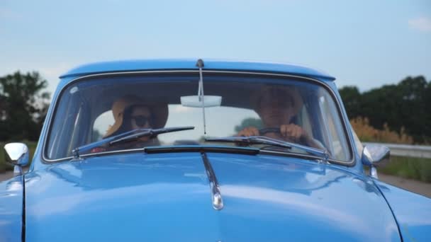 Pareja joven en sombreros montando en coche de época en los viajes de verano. Hombre y mujer sentados en el asiento delantero del viejo coche retro y hablando durante el viaje. Concepto de viaje por carretera en vacaciones. Cámara lenta Primer plano — Vídeo de stock