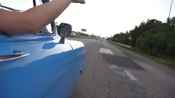 Brazo femenino fuera del coche retro jugando con el viento durante el viaje de verano. Mujer joven saludando con su mano en el viento en el viaje. Chica pone su brazo por la ventana del coche viejo para sentir la brisa. Movimiento lento — Vídeo de stock