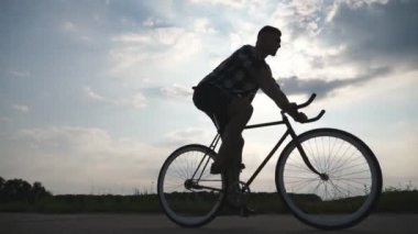 Genç adam arka plan güzel günbatımı gökyüzüne vintage bisiklet sürme silüeti. Sportif adam ülkede yol Bisiklete binme. Erkek bisikletçi sabit binicilik bisiklet dişli. Sağlıklı aktif yaşam tarzı portre