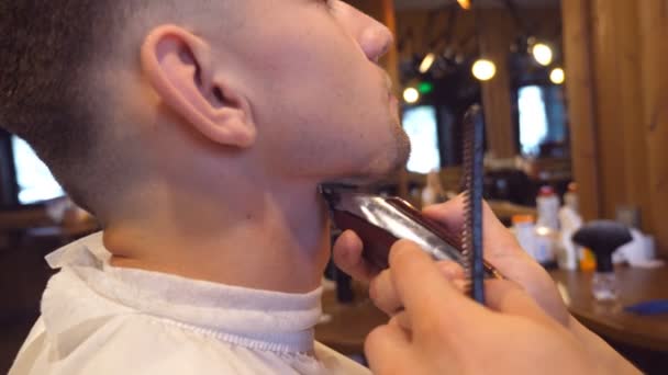 Trimming beard of male client with clipper at barber shop. Hairstyling process. Close up Slow motion — Stock Video