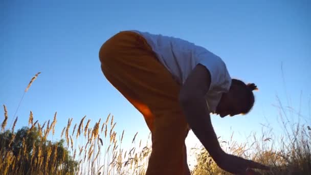 Primo piano di uomo sportivo in piedi a yoga posa al prato. Un ragazzo che si allena sulla natura. Atleta che fa esercizio sul campo. Cielo blu sullo sfondo. Concetto di sano stile di vita attivo. Vista ad angolo basso — Video Stock