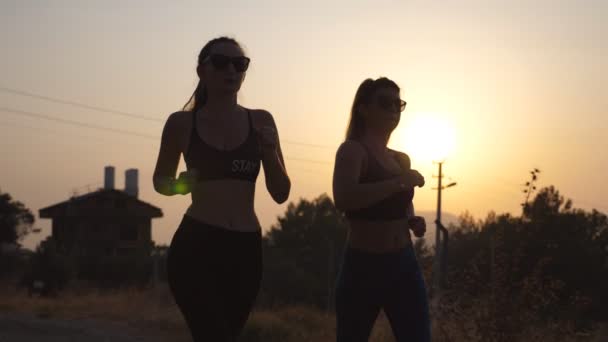 Dvě mladé dívky běží venku při západu slunce. Mladé ženy sportovní jogging na venkovské silnici. Atletky trénink společně v přírodě. Zdravý aktivní životní styl zpomalené