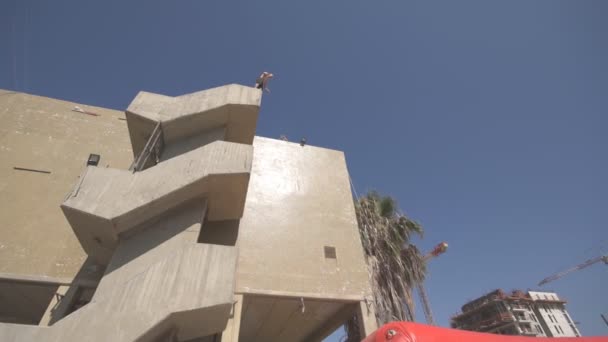 Вид збоку на невпізнаваного чоловіка, який стрибає з високої будівлі і падає в надувний батут в сонячний день. Концепція здорового способу життя. Крупним планом Повільний рух — стокове відео