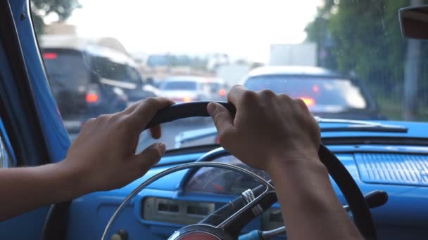 Close up of male hands holding on a steering wheel of old retro car and nervously tapping fingers. Unrecognizable man standing in traffic jam at downtown. POV Slow motion — Stock Video