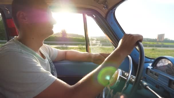 Perfil del joven cogido de la mano en el volante y conduciendo un coche retro con destello de sol en el fondo. Hombre caucásico viajando en un vehículo de época en el campo. Vista lateral cámara lenta Primer plano — Vídeos de Stock