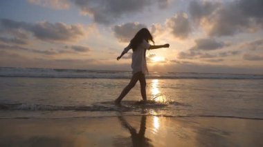 Okyanus sahilde yürüyüş ve ayakları ile su püskürtme tanınmaz halde kadın. Genç güzel kız hayattan zevk ve deniz sahilinde eğleniyor. Yaz tatili. Arka plan günbatımında. Ağır çekim