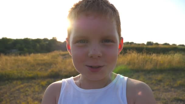 Adorable beau bébé regardant dans la caméra avec un sourire joyeux. Gros plan sur les émotions de l'enfant mâle avec une expression heureuse sur le visage. Portrait de garçon aux cheveux roux heureux avec des taches de rousseur rit en plein air. Mouvement lent — Video