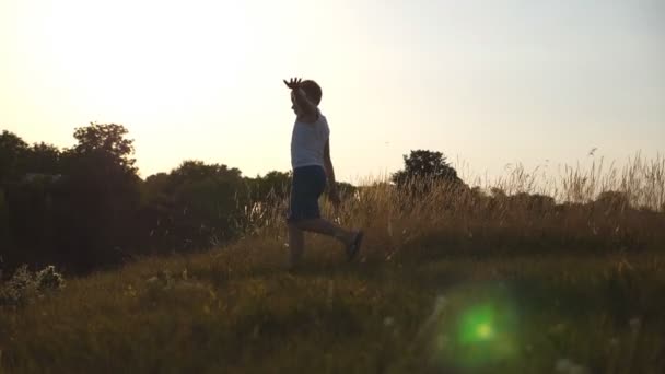 Молодий хлопець з піднятими руками літака біжить на зеленій траві на полі в сонячний день. Дитина біжить на галявині на відкритому повітрі. Щасливий чоловік розважається в природі на літньому лузі. Повільний рух крупним планом — стокове відео