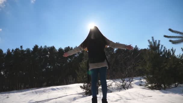 年轻的女孩站在一个冬季森林的背景和举起她的胳膊。妇女享受冬季景观。自由概念。慢动作关闭 — 图库视频影像