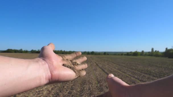 Mãos de agricultor masculino segura um punhado de terra seca e verifica a fertilidade do solo no campo. Braços de jovem derramando terra através de seus dedos no prado. Conceito de agricultura. POV Movimento lento — Vídeo de Stock