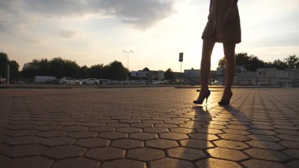 Жіночі ноги на високих підборах взуття, що йде по міській вулиці на заході сонця. Ноги молодої ділової жінки на високих підборах взуття йдуть в місто з сонячним спалахом на фоні. Дівчина ступає. Повільний рух — стокове відео