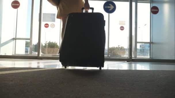 Woman in heels goes to exit from airport and roll suitcase on wheels. Girl walking with her suitcase along airport hall or waiting room. Business lady going with her luggage. Travel concept Slowmotion — Stock Video