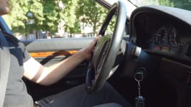 Tanınmayan adam onun elinde direksiyon simidinde el ve güneşli yaz gününde kentsel yolda bir araba kullanıyor. Genç adam arabasına biniyor. Yan görünümü ağır çekim kapatın